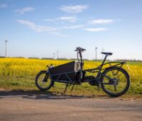 Ein Lastenrad vor einem Rapsfeld udn Windturbinen im Hintergrund.