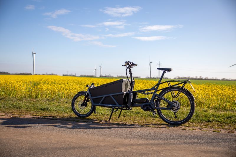 Ein Lastenrad vor einem Rapsfeld udn Windturbinen im Hintergrund.