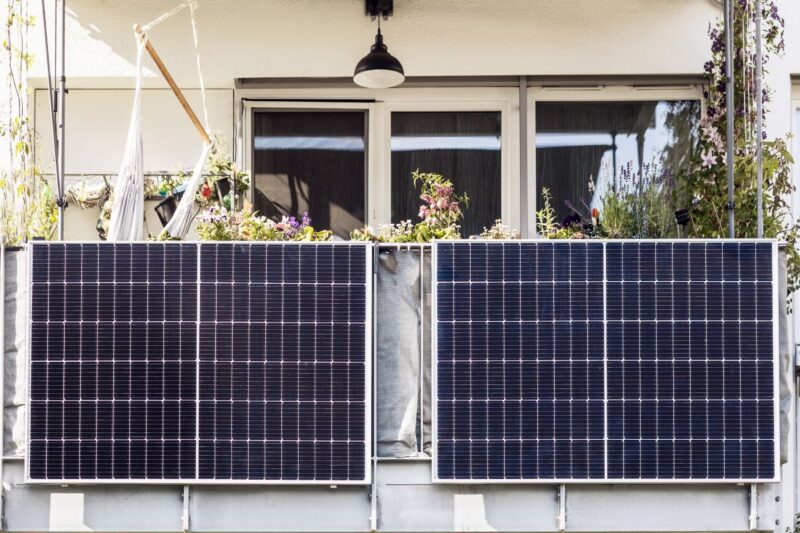 Zwei Solarmodule an einem mit Blumen bepflanzten Balkon.