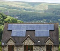 Eine alte PV-Dachanlage auf einem alten Haus in grün-hügeloger Umgebung.