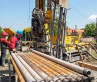 Zwei Arbeiter, viele Rohre: das Bild zeigt eine Geothermiebohrung.