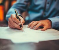 Person im Business-Hemd schreibt auf Formularen.