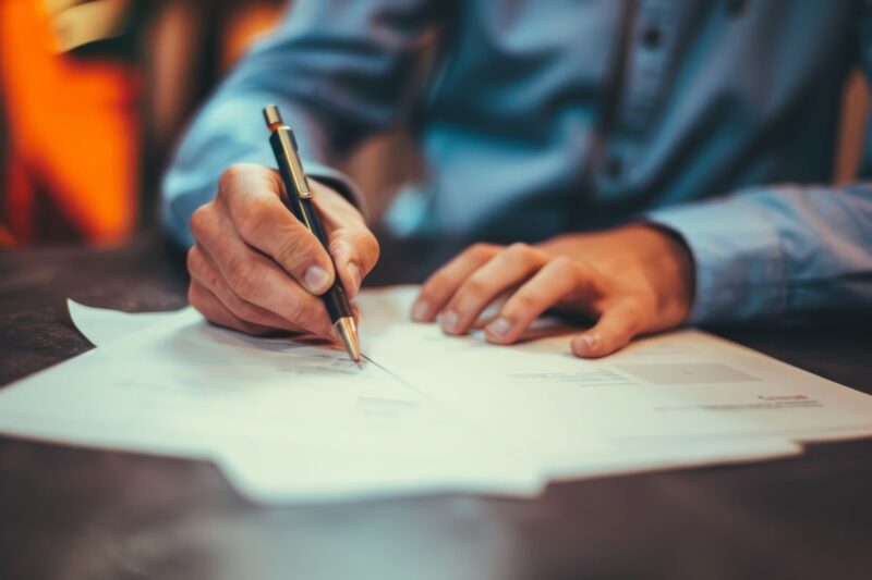 Person im Business-Hemd schreibt auf Formularen.