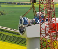 Eine Windgondel bei der Montage hoch über Feldern.