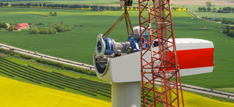 Eine Windgondel bei der Montage hoch über Feldern.