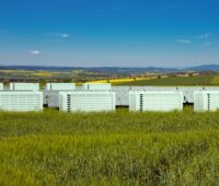 Eine Reihe von Batteriecontainern mit Solarpaneelen auf grüner Wiese.