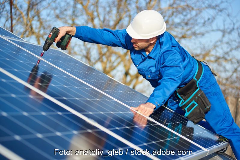 Ein Arbeiter im Blaumann montiert Solarmodule.