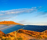 Aufgeständerte Solarpanels über rotrer Erde bei blauem Himmel.