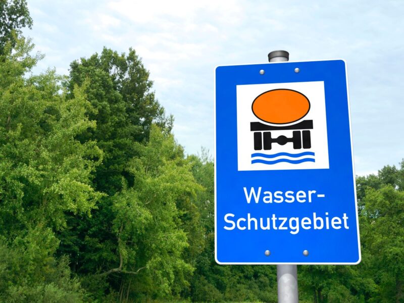 Hinweisschild für Wasserschutzgebiet vor grünen Bäumen.