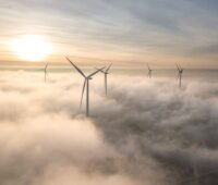 Windenergieanlagen an Land bei Sonnenaufgang und aufsteigendem Dunst.