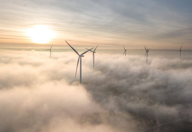 Windenergieanlagen an Land bei Sonnenaufgang und aufsteigendem Dunst.