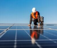 Arbeiter mit Schutzhelm und Weste montiert auf einem Flachdach Solarmodule