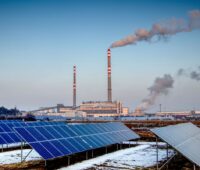 Solarpark in der Umgebung einer Industrieanlage mit rauchenden Schloten.