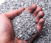 Silber- (oder Aluminium-)pellets in einer Hand. Symbolbild für Silber als wertvollen Rohstoff.