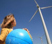 Symbolbild: ein Kind mit Globus in der Hand blickt auf eine Windenergieanlage