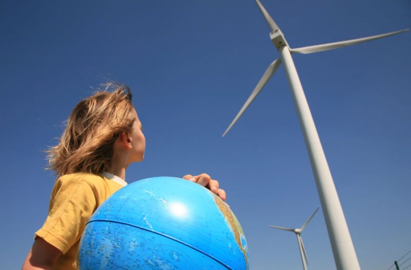 Symbolbild: ein Kind mit Globus in der Hand blickt auf eine Windenergieanlage