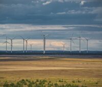 Windräder in flacher Landschaft auf braunem Boden vor Wolken.