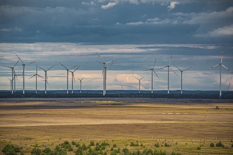 Windräder in flacher Landschaft auf braunem Boden vor Wolken.