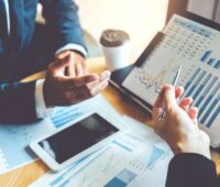 Businesshände und ein Laptop mit Finanzzahlen.