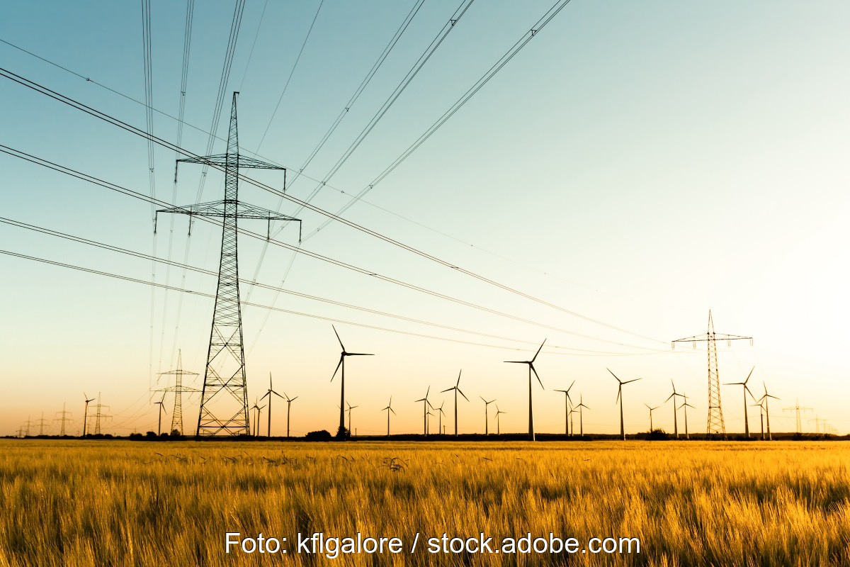 Stromnetz mit Feld und Windpark im Hintergrund bei Sonnenuntergang.