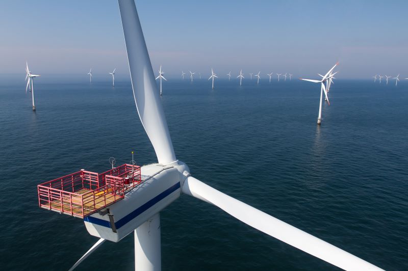 Blick über einen Offshore-Windpark aus der Vogelperspektive, im Vordergrund links eine Windturbine und Rotoren.