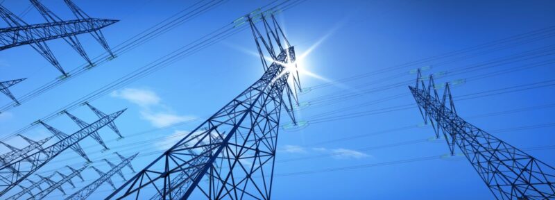 Strommasten vor Sonne am blauem Himmel.