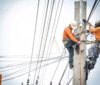 Zwei Arbeiter auf einem Strommast mit Leitungen in vielen Richtungen - Symbol für Stromnetz