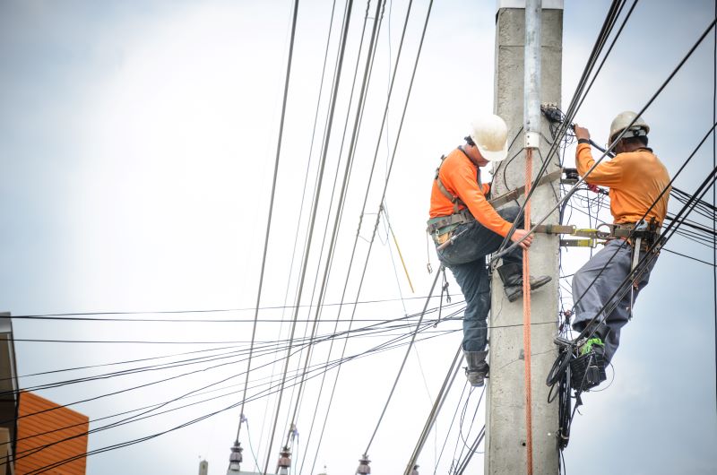 Zwei Arbeiter auf einem Strommast mit Leitungen in vielen Richtungen - Symbol für Stromnetz