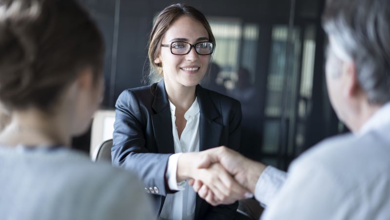 Eine junge Frau im Businesslook schüttelt einem Kunden die Hand.