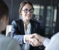 Eine junge Frau im Businesslook schüttelt einem Kunden die Hand.