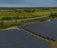 Freiflächen-Solarpark im Flachland an der Autobahn, am Horizont Windanlagen.