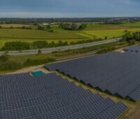 Freiflächen-Solarpark im Flachland an der Autobahn, am Horizont Windanlagen.