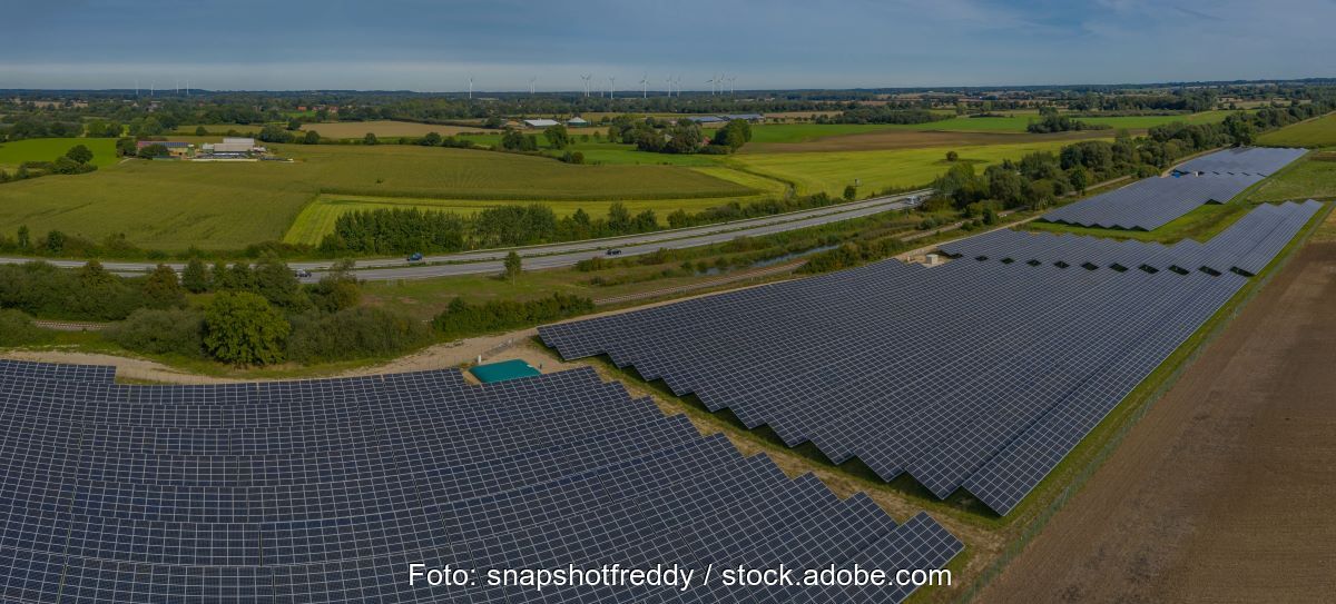 Freiflächen-Solarpark im Flachland an der Autobahn, am Horizont Windanlagen.