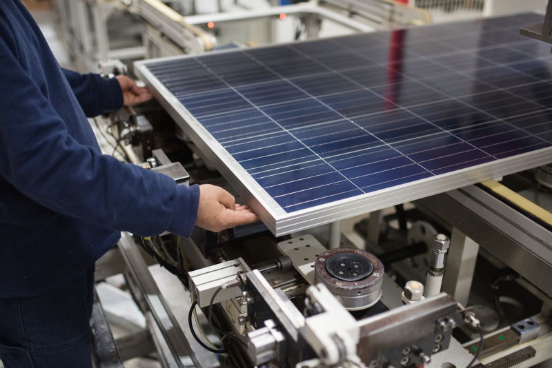 Arbeiter mit einem Solarmodul in einer Fabrik an einer Maschine.