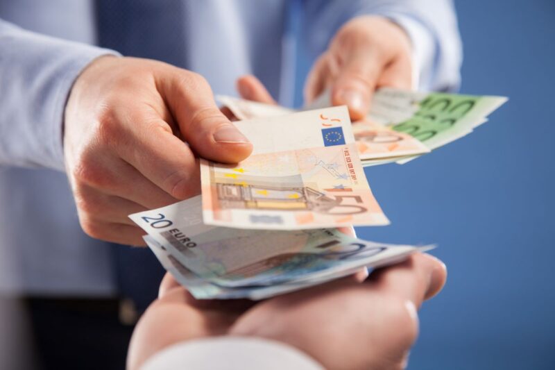 Die Hände einer Person zählen Geldscheine in die Hände einer zweiten Person.
