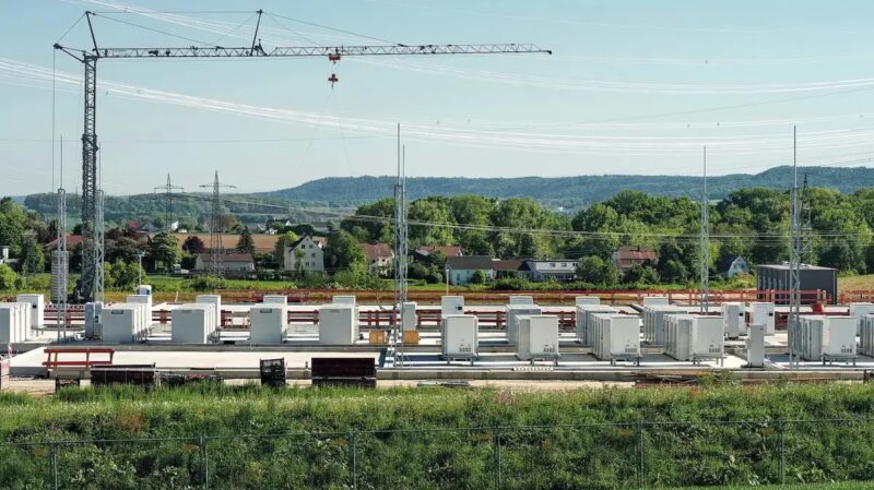 Kräne und Container auf grüner Wiese, ein Großbatteriespeicher-Park im Bau.