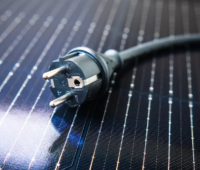 Ein Anschlusskabel mit Stecker liegt auf Solarmodulen, die Clearingstelle EEG|KWKG gibt Antwort auf die Frage, was beim Anschluss von Stecker-Solargeräten (Balkonkraftwerke) zu beachten ist.