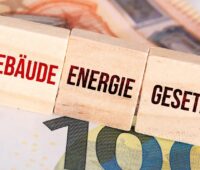 Drei Holzwürfel mit der Aufschrift Gebäudeenergiegesetz liegen auf Euro-Banknoten. Der geplante Nachfolger Gebäudemodernisierunsgesetz erfährt Kritik bei der Wärmepumpenförderung.