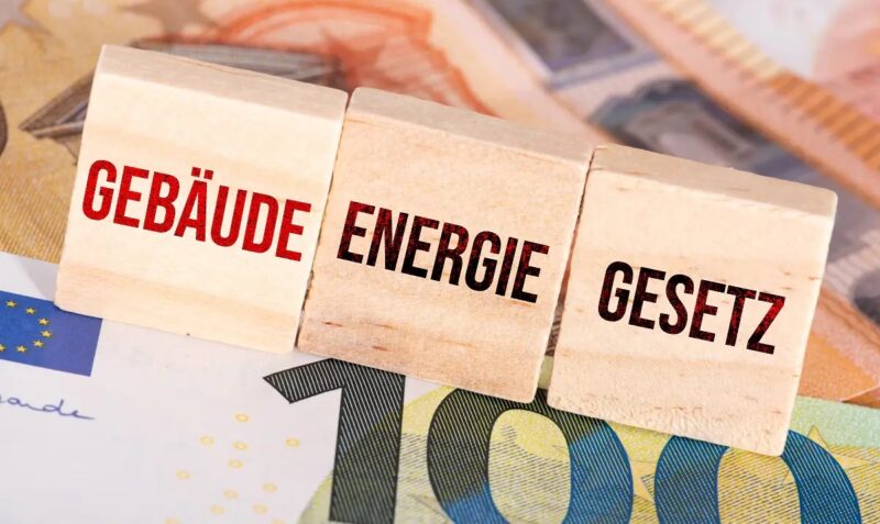Drei Holzwürfel mit der Aufschrift Gebäudeenergiegesetz liegen auf Euro-Banknoten. Der geplante Nachfolger Gebäudemodernisierunsgesetz erfährt Kritik bei der Wärmepumpenförderung.