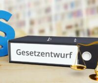 Ordner mit Aufschrift "Gesetzesentwurf", Paragrafenzeichen und Waage als Symbol für das geplante Netzpaket.