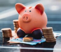Ein Sparschwein mit Geld auf einem Solarmodul, Vattenfall bietet eine Finanzierung für Photovoltaik-Anlagen und Wärmepumpen an.