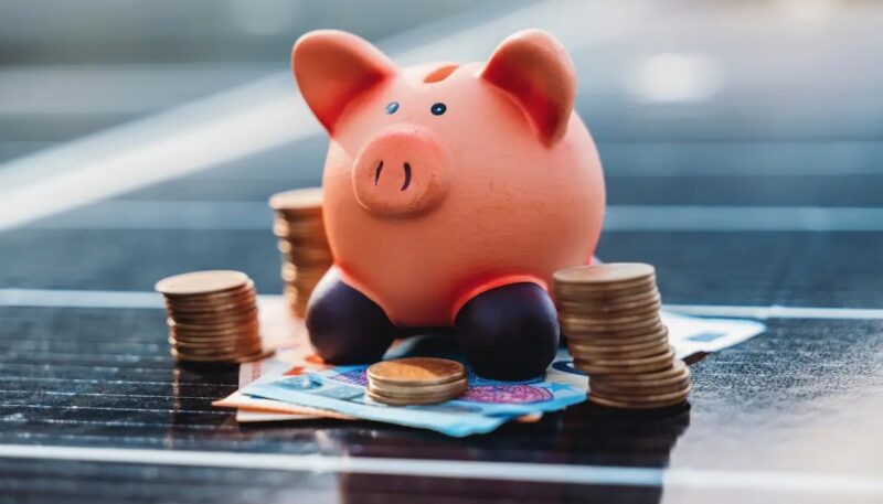 Ein Sparschwein mit Geld auf einem Solarmodul, Vattenfall bietet eine Finanzierung für Photovoltaik-Anlagen und Wärmepumpen an.