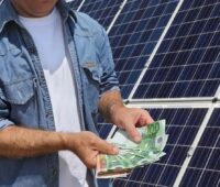 Ein Mann mit Geldscheinen vor Solarmodulen, die Bundesnetzagentur will in der Agnes Netzentgeltreform einen Prosumer-Aufschlag für Photovoltaik-Anlagen einführen.
