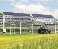 Traktor fährt unter den Solarmodulen einer Agri-PV-Anlage her.