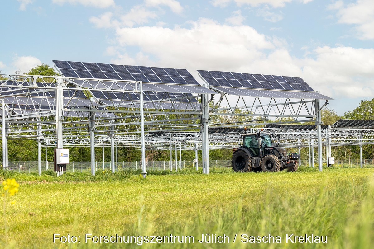 Traktor fährt unter den Solarmodulen einer Agri-PV-Anlage her.
