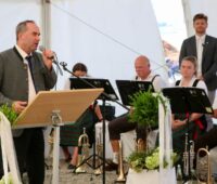 Hubert Aiwanger mit Mikrofon, eine Blaskappelle im Hintergrund - Feier am Bürgerwindpark in Bayern