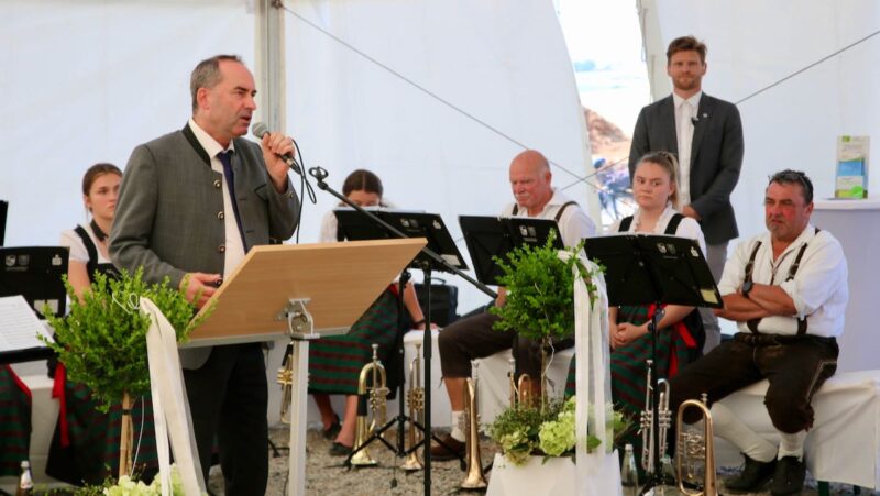 Hubert Aiwanger mit Mikrofon, eine Blaskappelle im Hintergrund - Feier am Bürgerwindpark in Bayern