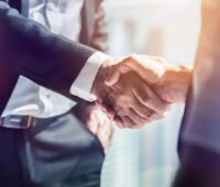 Das Bild zeigt im Anschnitt einen Handschlag zwischen zwei Männern in Anzügen als Symbolbild für eine Einigung.