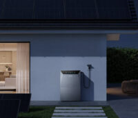 Zu sehen ist die neue Solarbank 4 Pro vor einer Hauswand bei Nacht. Links von dem Batteriespeicher steht auf dem Rasen eine PV-Balkon-Anlage.