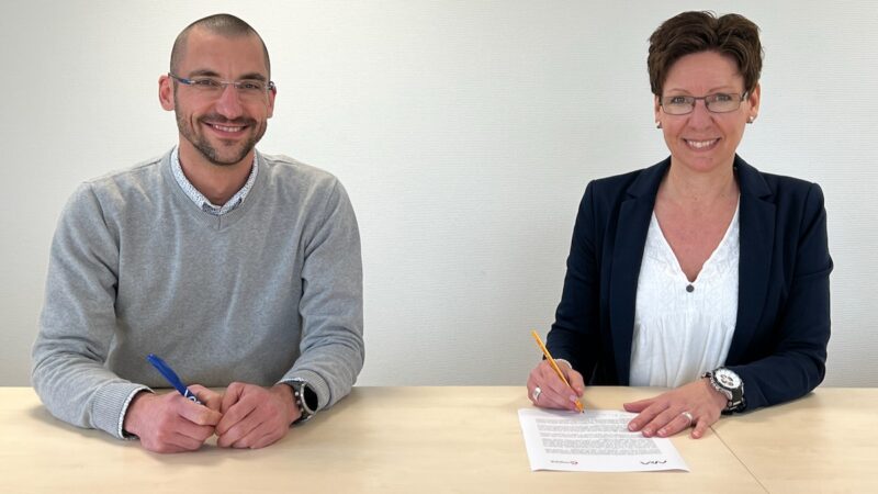Ein Mann und eine Frau an einem Tisch, sie unterschreibt den Lizenz-Vertrag für die OPV-Technologie.